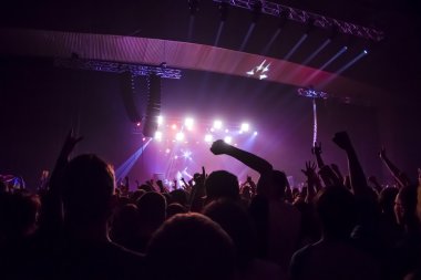Parlak sahne ışıkları önünde konser kalabalığının siluetleri