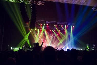 Parlak sahne ışıkları önünde konser kalabalığının siluetleri