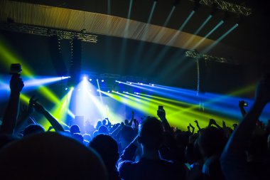 Parlak sahne ışıkları önünde konser kalabalığının siluetleri