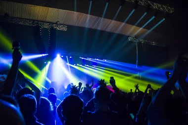 Parlak sahne ışıkları önünde konser kalabalığının siluetleri