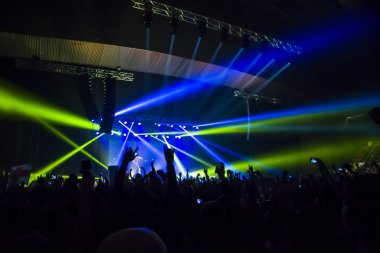 Parlak sahne ışıkları önünde konser kalabalığının siluetleri
