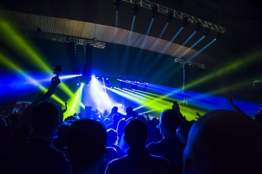 Parlak sahne ışıkları önünde konser kalabalığının siluetleri