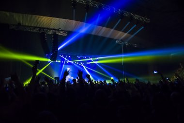 Parlak sahne ışıkları önünde konser kalabalığının siluetleri