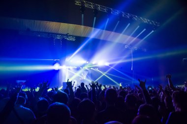 Parlak sahne ışıkları önünde konser kalabalığının siluetleri