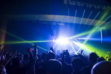 Parlak sahne ışıkları önünde konser kalabalığının siluetleri