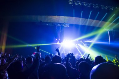 Parlak sahne ışıkları önünde konser kalabalığının siluetleri