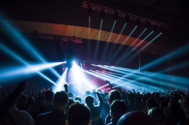 Parlak sahne ışıkları önünde konser kalabalığının siluetleri