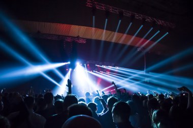 Parlak sahne ışıkları önünde konser kalabalığının siluetleri
