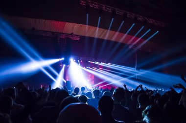Parlak sahne ışıkları önünde konser kalabalığının siluetleri