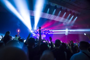 Parlak sahne ışıkları önünde konser kalabalığının siluetleri