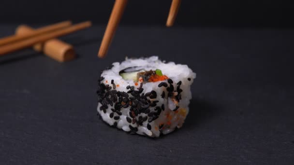 Sticks Take Sushi chopsticks κοντινό. νόστιμα ιαπωνικά ρολά σούσι με σπόρους σουσαμιού σε μια πέτρινη σανίδα σε μαύρο — Αρχείο Βίντεο