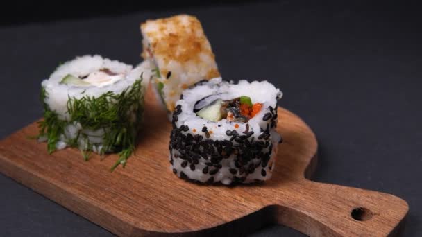 Délicieux rouleaux de sushi japonais avec des graines de sésame sur une planche de pierre sur un noir — Video