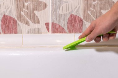 removing old dirty silicone from bathtub in a washroom clipart