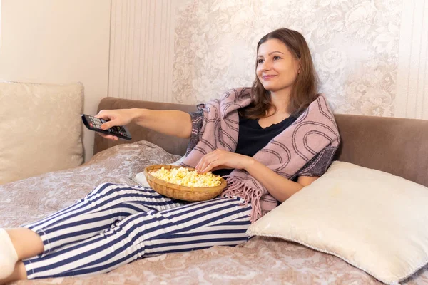 cheerful young girl with popcorn bowl sitting on sofa. Watching tv movie funny comedy talk show program.