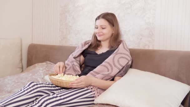 Jeune femme assise dans le canapé, regarder la télévision, changer de chaînes avec une télécommande — Video