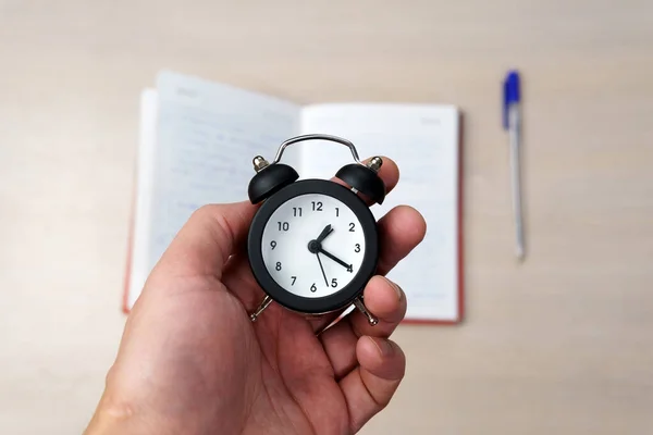 man holds alarm clock in hand alarm clock on books for study, work and time management concept