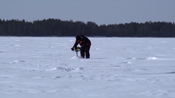 Visser op een winter plas boor het ijs met een motor boor — Stockvideo