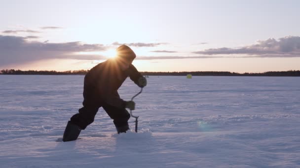 Fisher drills a hole in the ice. Winter fishing on the background of a frozen lake. — Stock Video