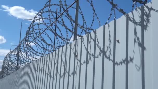 Kovový plot s ostnatým drátem na pozadí modré oblohy. — Stock video
