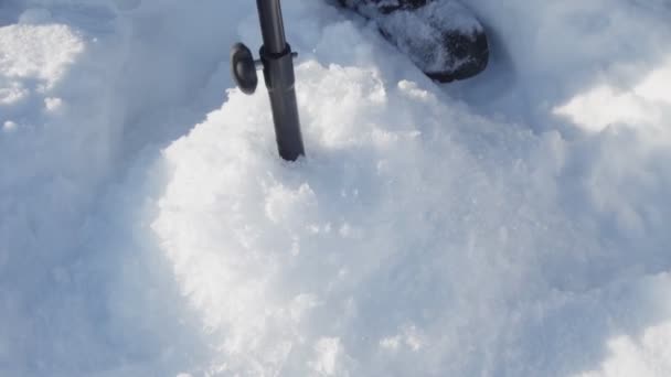 Muž vyvrtá díry do ledu, aby lovil na ledě s pohrabáčem. selektivní zaměření — Stock video