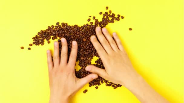 Kaffebönor på en gul bakgrund blandas av händerna på en man. Ovanifrån. stoppa rörelse — Stockvideo