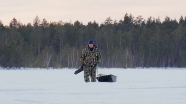 Mężczyzna rybak spacery po jeziorze z lodu wiertarka i sprzęt wędkarski. — Wideo stockowe