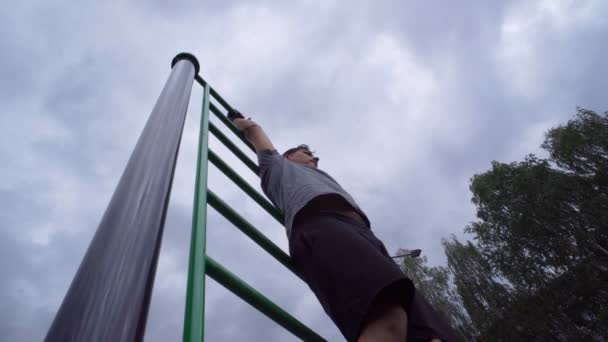 Man trains on the street on a horizontal bar. Playing sports in the fresh air. — Stock Video