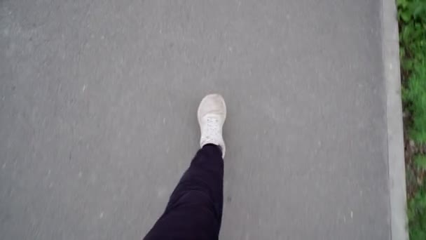 Un hombre está caminando sobre el asfalto en zapatillas blancas y pantalones negros. Enfoque selectivo — Vídeos de Stock