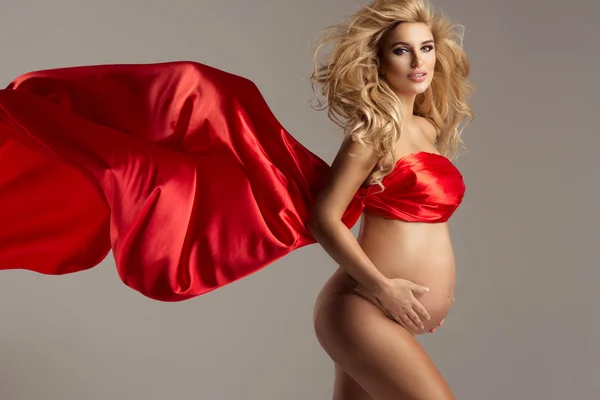 Элегантная беременная мама с волнистым красным платьем позирует в гордости за свою беременность — стоковое фото