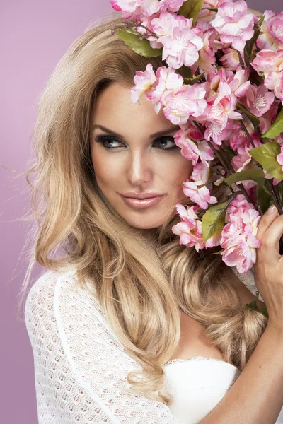 Glamorous curvy blonde woman with a sexy body posing with flowers on a pink studio background. — Stock Photo, Image