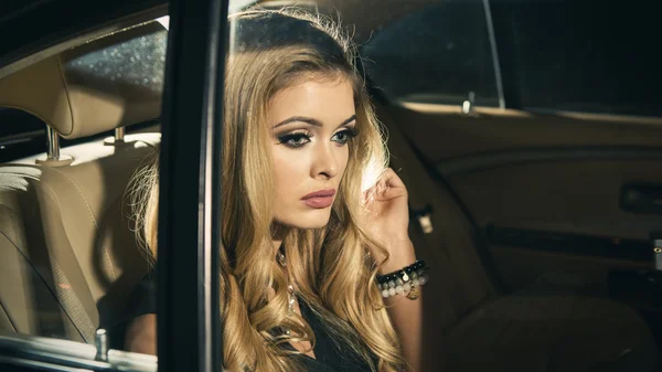 Joven mujer rubia sentada en el asiento trasero de un coche de lujo por la noche — Foto de Stock