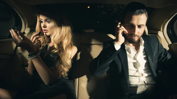 Sexy couple in the car. Young woman applying lipstick and man using cell phone in car. — Stock Photo, Image