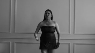 Beyaz bir duvarın karşısında dans eden elbise giymiş bir kızın portresi.