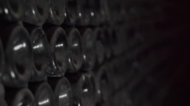 Close up shot of Wine bottles lying in stack at cellar. Glass bottles of red wine stored in wooden shelving in stone cellar. Interior underground wine cellar in winery — Stock Video