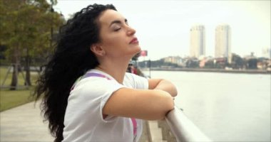 Parktaki nehrin kıyısında duran güzel esmer bir kadının portresi. Kız gözlerini kapar, kameraya bakar, rahat bir ruh hali gösterir..