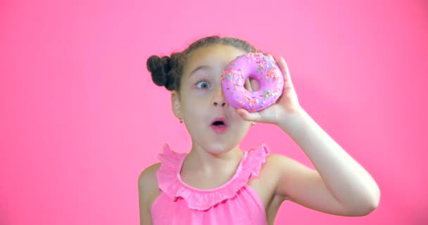 Menina atraente bonito segurando donuts com cobertura para as mãos sorrindo olha para a câmera e traz-los para o rosto olhando para olhar para a coleção de donuts doces com cobertura rosa. Retrato criança — Vídeo de Stock