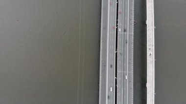 Şehir köprüsünün üzerinde, güzel deniz okyanusu ve büyük şehir binalarının zeminine karşı arabalar ve motorsikletlerle uçan hava aracı manzarası. Köprü ve şehir otoyolu.