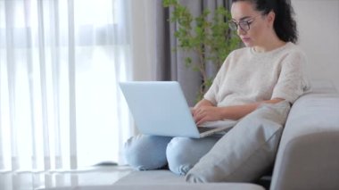 Dizüstü bilgisayarda çalışan bir kadın, evdeki koltukta oturan bir iş kadını, evde oturup laptopta ya da akıllı telefon kontrolleriyle evde çalışmak için posta kontrol ediyor..
