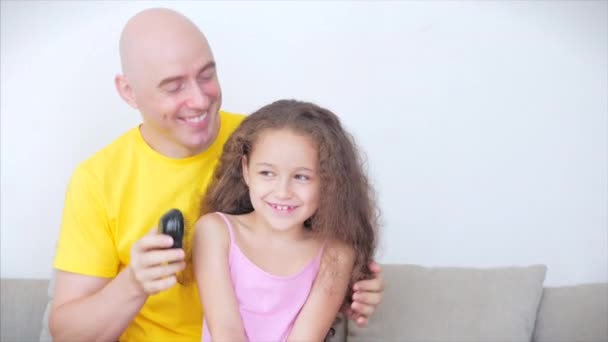 Dad sits at home on the couch, does his hair, combing the hair of his cute little daughter, the child rejoices in dads care of her. — Stock Video