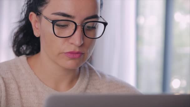 Joven mujer seria freelancer trabajando en una computadora portátil sentada en un sofá en casa, mujer de negocios escribiendo en una computadora portátil, chica enfocada usando una computadora para estudiar trabajo en línea en casa. Concepto de trabajo del empleado doméstico — Vídeos de Stock