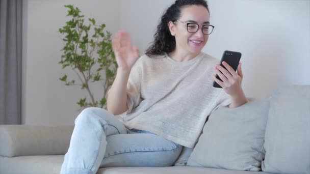 Mutlu genç kadın serbest çalışan kamera konuşmalarına bak canlı yayında iş ile ilgili konferanslar yap. Bilgisayar uygulaması kayıt günlüğü kullanan bir kız evdeki kanepede oturuyor. — Stok video