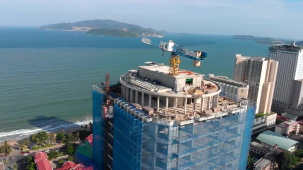 Fotografia aérea drone permite admirar uma bela vista da cidade e a construção de um edifício alto contra o pano de fundo de belos arranha-céus ou o mar azul. VIETNAM, NHA TRANG — Vídeo de Stock