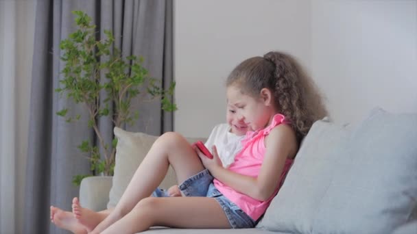 Crianças felizes brincando em casa relaxante usar um smartphone abraçando sentar-se no sofá filha e filho, olhar para a tela de um telefone celular, assistir desenhos animados. — Vídeo de Stock