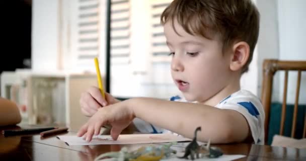 Glad liten pojke eller söt grundskolebarn i åldern 7-8 år hemma avkopplande sitter i huset och färger på papper använda färgpennor. Barn drar, fokuserade barn grundläggande utbildning koncept. — Stockvideo