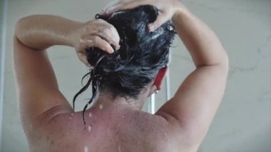 Güzel genç bir kadın sıcak bir duş deresinin altında durarak saçındaki şampuanı temizler. Saç ve vücut temizliği kavramı, hijyen..