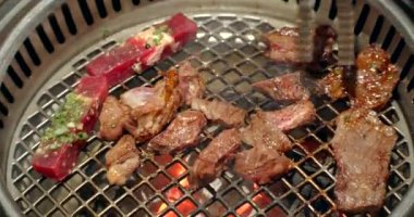 Şef tong 'u kullanıyor ve eti ızgaraya çeviriyor. Ateş yanıyor, yağlı biftek yavaş çekimde pişiyor. Izgara, lezzetli biftek yavaş çekimde yakın çekim..