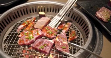 Şef tong 'u kullanıyor ve eti ızgaraya çeviriyor. Ateş yanıyor, yağlı biftek yavaş çekimde pişiyor. Izgara, lezzetli biftek yavaş çekimde yakın çekim..