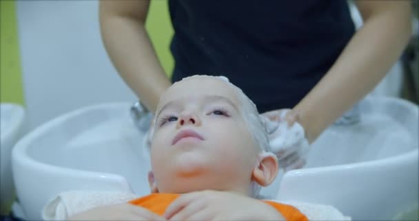 Parekhmacher, après avoir coupé les cheveux d'un enfant d'âge préscolaire, se laver les cheveux, savon avec shampooing, enfant se couche au repos et profite pendant qu'ils se lavent les cheveux après qu'ils ont leur coupe de cheveux. — Video