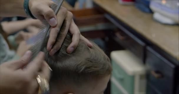 Kinderhaarstyling. Stylist in einer Schutzmaske von covid-19 macht eine stylische Frisur. Kinderfrisur im Salon zur Zeit der Coronavirus-Epidemie. Kleiner Junge bekommt einen Haarschnitt. — Stockvideo