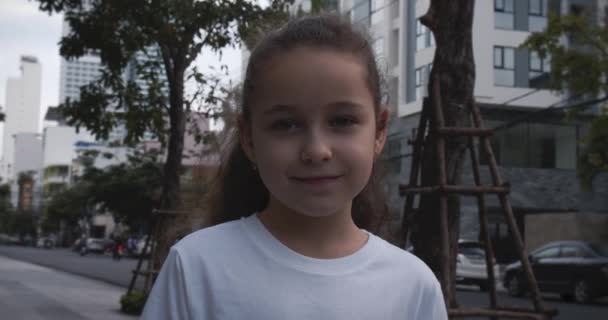 Porträt Lustiges kleines Mädchen lächelndes Kind, das am Sommertag auf der Straße in der Stadt in die Kamera blickt. Young Happy Nettes Kind mit hübschem Gesicht, das auf der Straße steht. Konzept einer glücklichen Kindheit. — Stockvideo